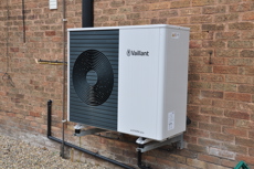 Close up of an air source heat pump which is attached to the side of a brick wall.